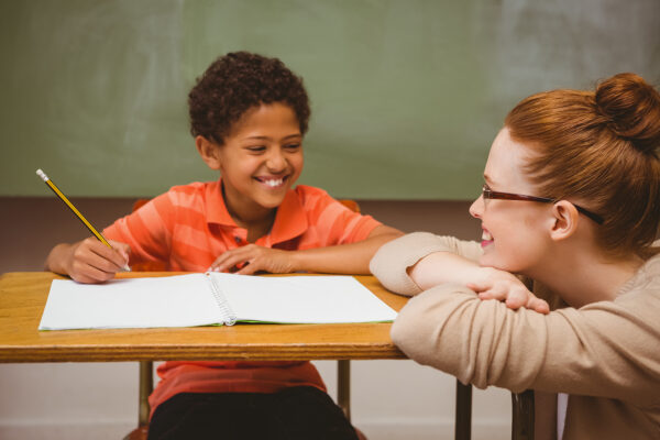 Portrait of teacher assisting little boy with homework in the classroom
